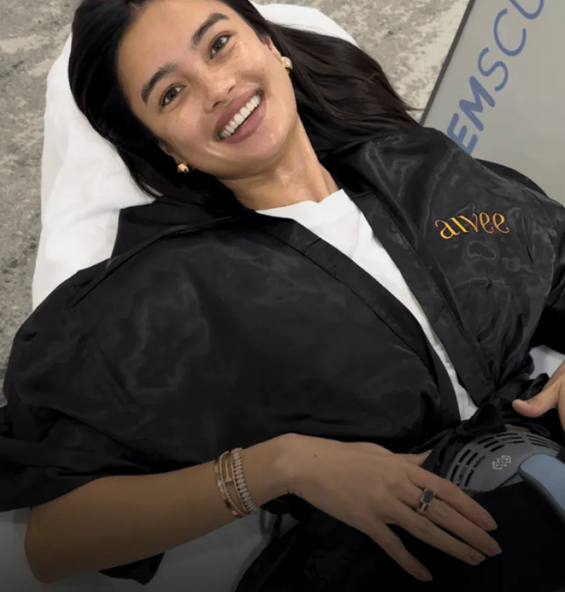 A smiling client in a black robe during an Aivee Emsculpt Neo body contouring session