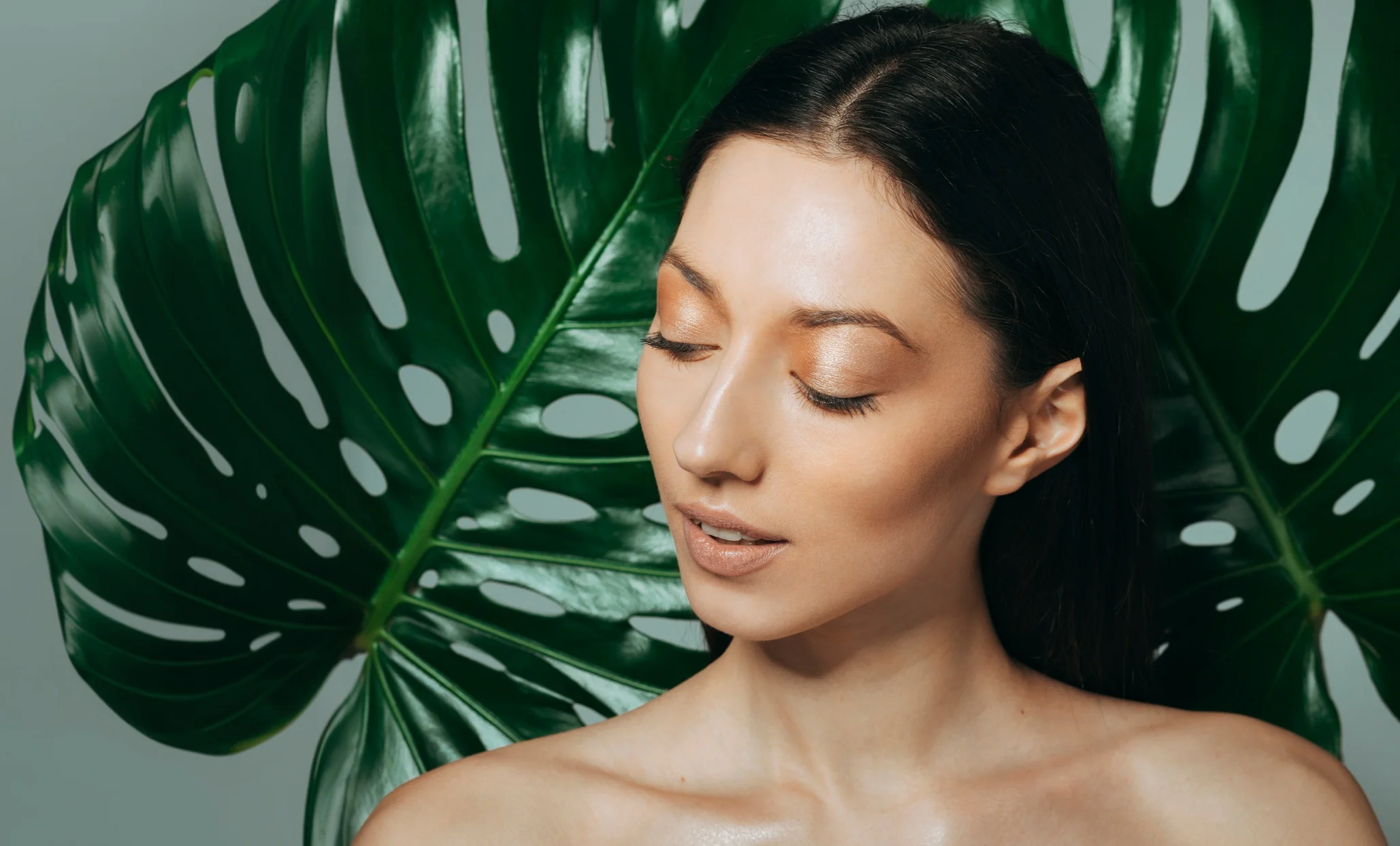Model with radiant glass skin framed by tropical leaves