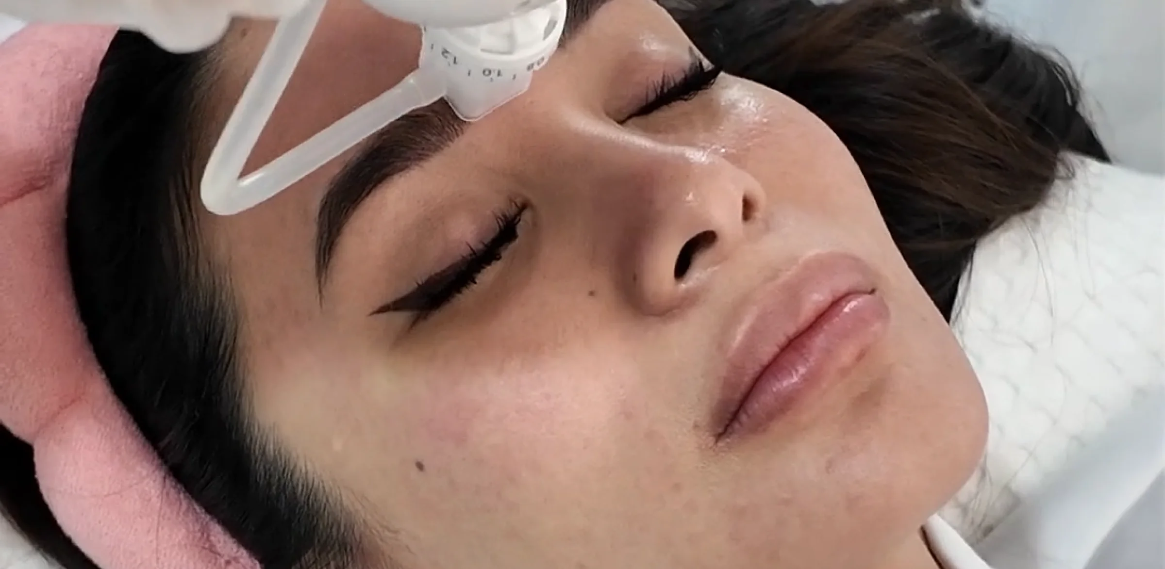 A client resting under a facial treatment device during an Aivee Dermashine session